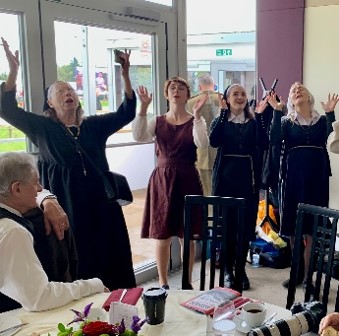 Women sing with raised hands at a bright indoor gathering