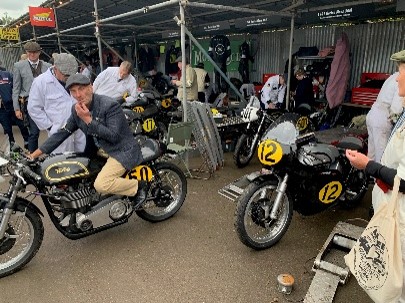 Riders and crew gather around vintage black-and-gold racing motorcycles