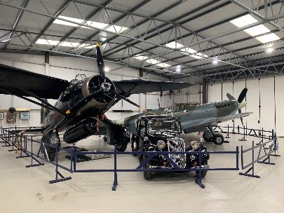 Museum hangar display featuring a black vintage aircraft, a gray-green plane