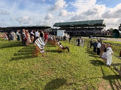 Visitors in period clothing gather on a sunny racecourse lawn