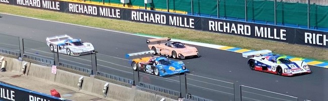 Colorful race cars speed down a circuit beside the pit wall